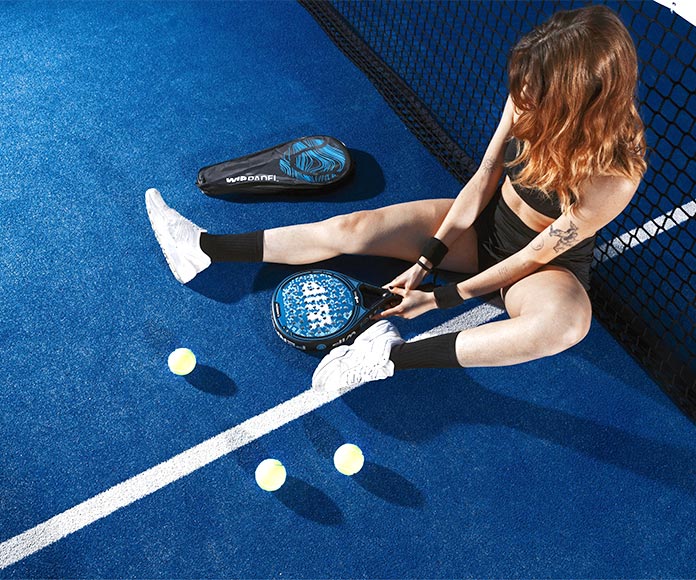 Mujer sentada contra la red en una pista de padel