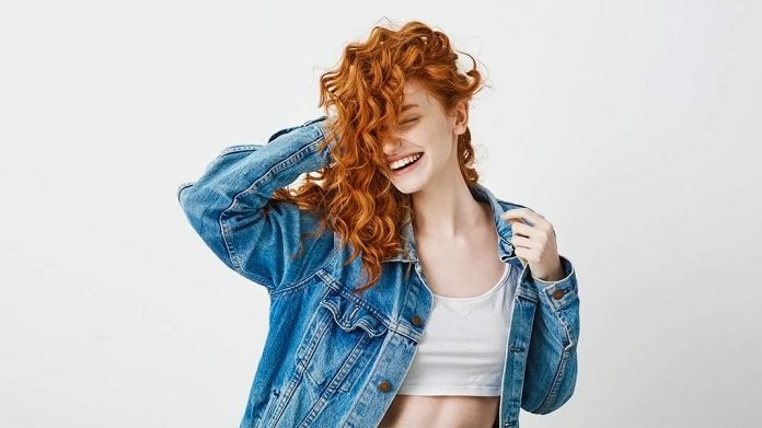 chica pelirroja de pelo rizado sonriendo y tocándose el cabello