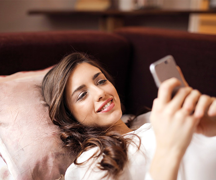 Mujer joven tumbada consultando su móvil