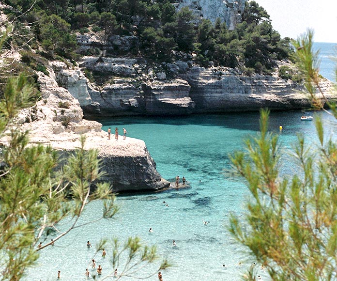 Playa o cala con gente bañándose en en el mar pleno verano.