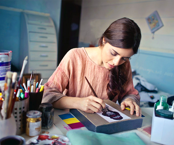 Mujer dibujando un cuadro con materiales de diseño alrededor