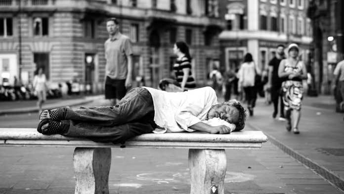Vagabundo durmiendo en un banco en la calle. Pobreza, exclusión social