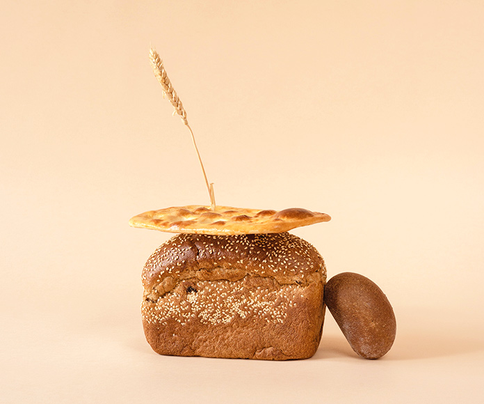 Composición conceptual del gluten: tres tipos de panes con una hebra de trigo detrás.