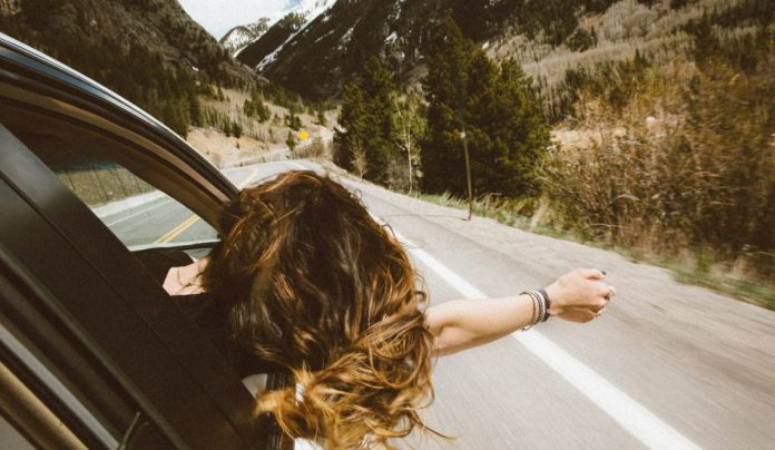 Mujer sacando la cabeza por la ventana de un coche viajando por carretera.