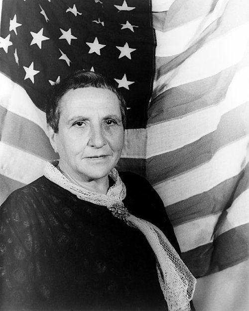 Gertrude posando con la bandera de Estados Unidos, foto en blanco y negro.