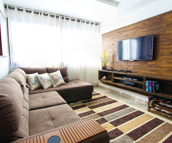 Salón con sofá en L y tv colgada en la pared sobre centro de entrenimiento