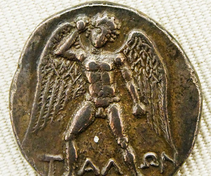 Talos esculpido en una moneda sosteniendo una piedra.