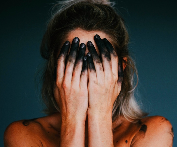 Mujer agobiada cubriendo su rostro con sus manos.