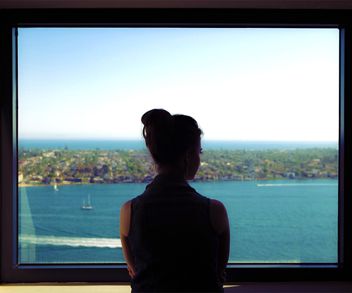 Mujer mirando por una ventana un paisaje costero