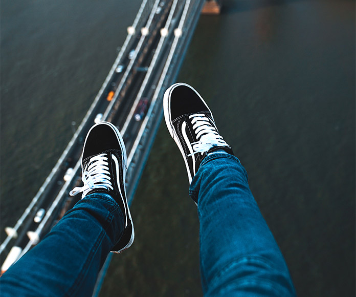 Persona en las alturas con unas zapatillas Vans y un puente al fondo